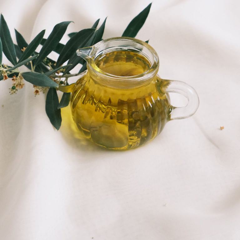 Pichet d'huile d'olive dorée et branche d'olivier sur un drapé clair